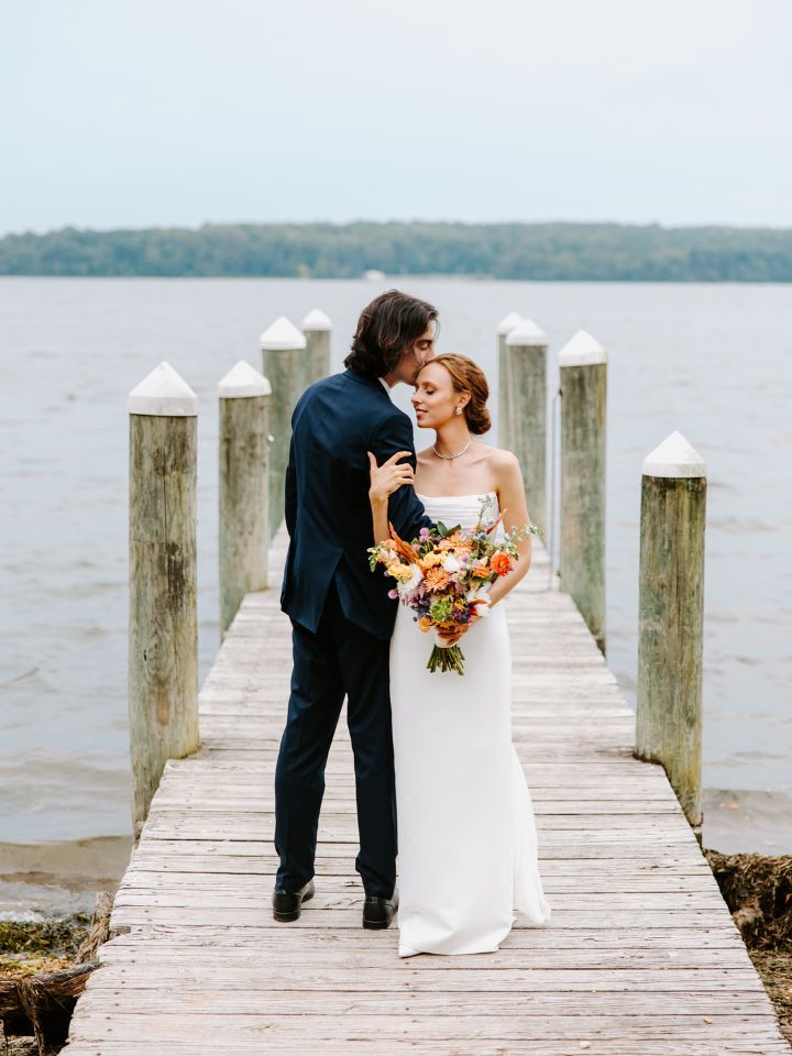 Bride and groom pose on a dock.