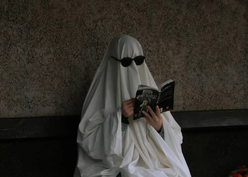 A client dressed up as a ghost reading a book with sunglasses on over the ghost costume