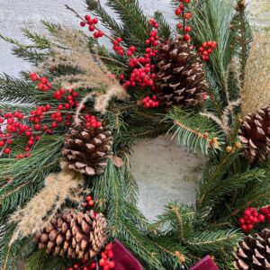 Closeup of a detail on an evergreen wreath with lots of dried grasses, red berries, and pine cones added in.