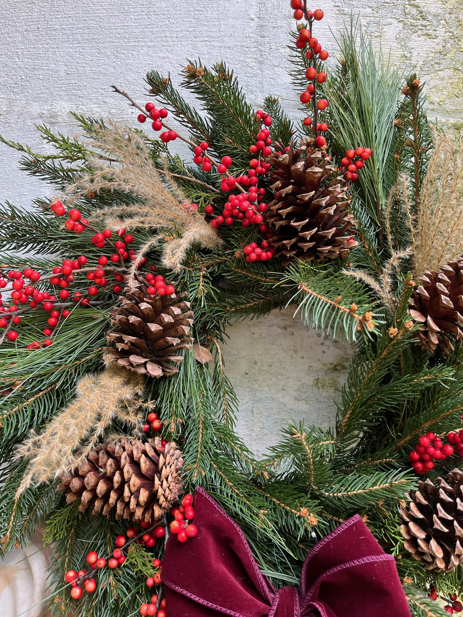 Closeup of a detail on an evergreen wreath with lots of dried grasses, red berries, and pine cones added in.