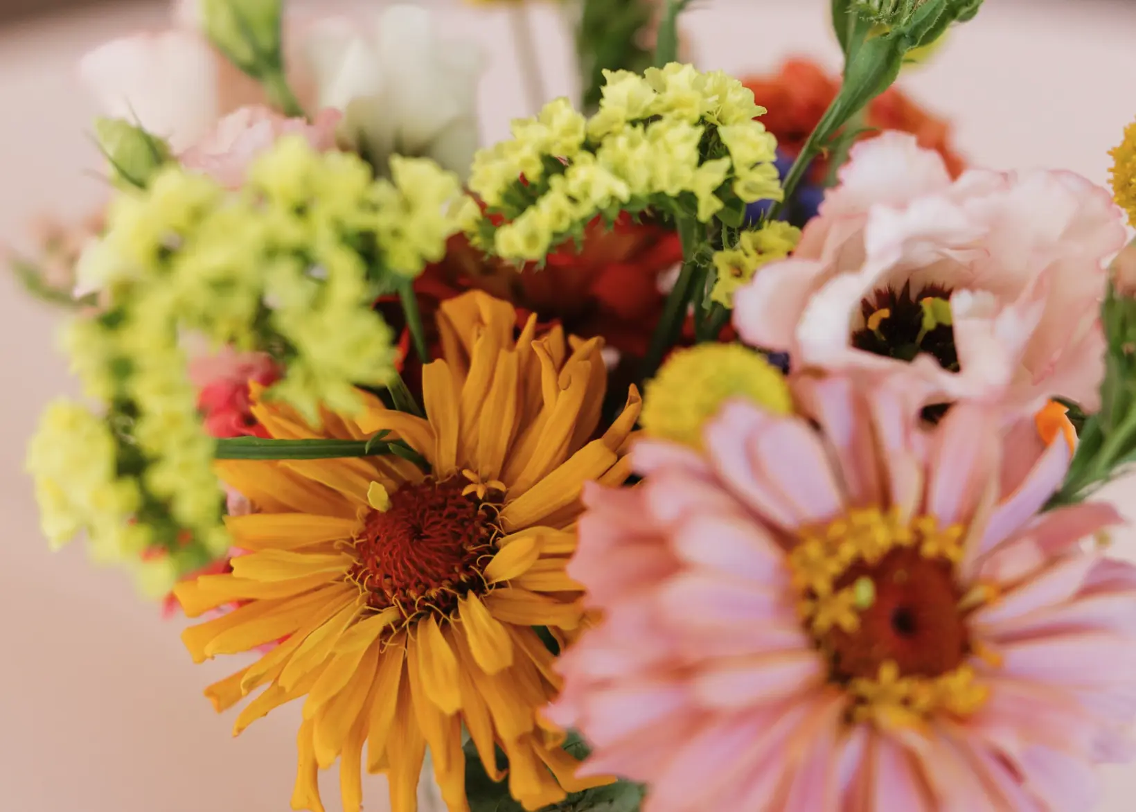 A jar arrangement of orange, yellow, and pink flowers up close