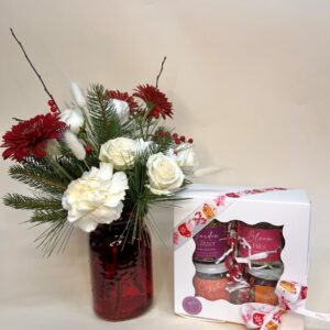 A red vase with Christmas flowers sits next to a white boxed gift set of edible floral petal sugars and salts.