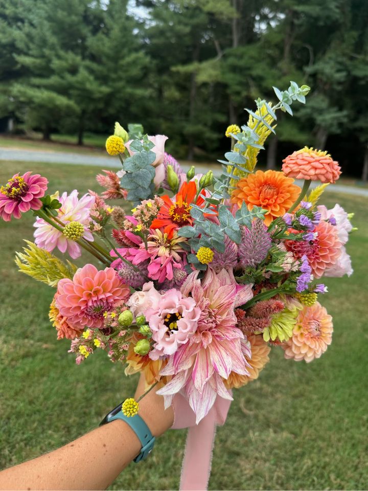 Bouquet of flower farm cut flowers held up in front of green trees.