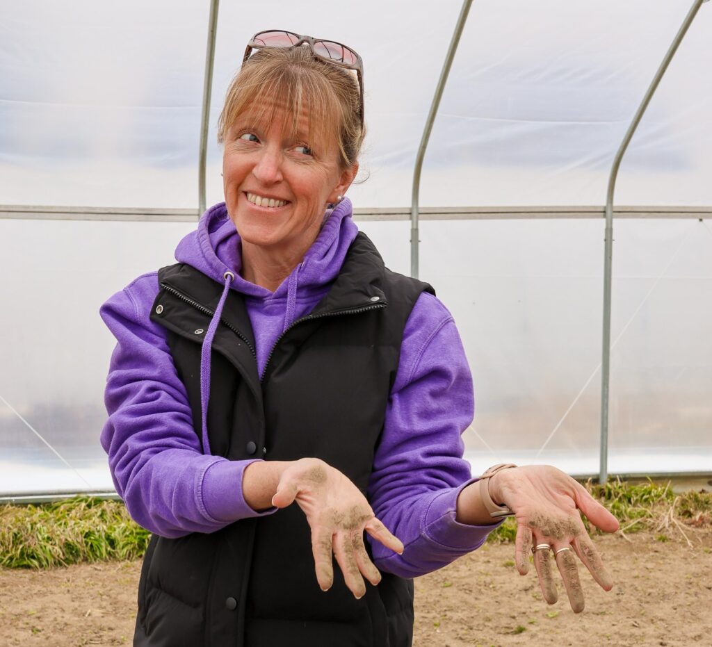 Liza holds out soil covered hands in the hoophouse.