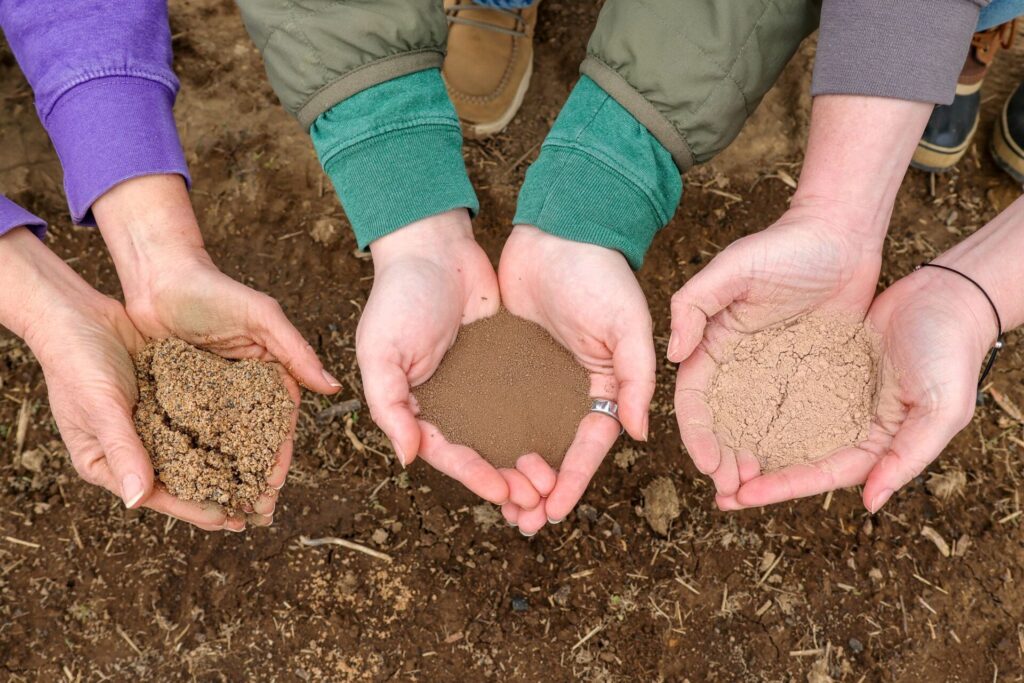 Three hands hold different types of soil.