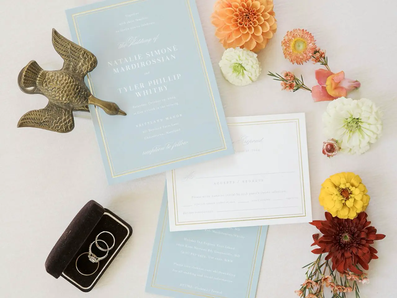 Wedding invitations in light baby blue up close with bright orange and coral flowers by Wildly Native Flower Farm