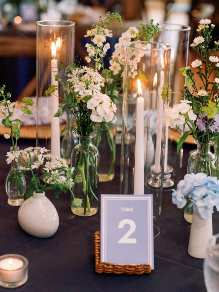 Bud vases and white taper candles on a navy blue table cloth.