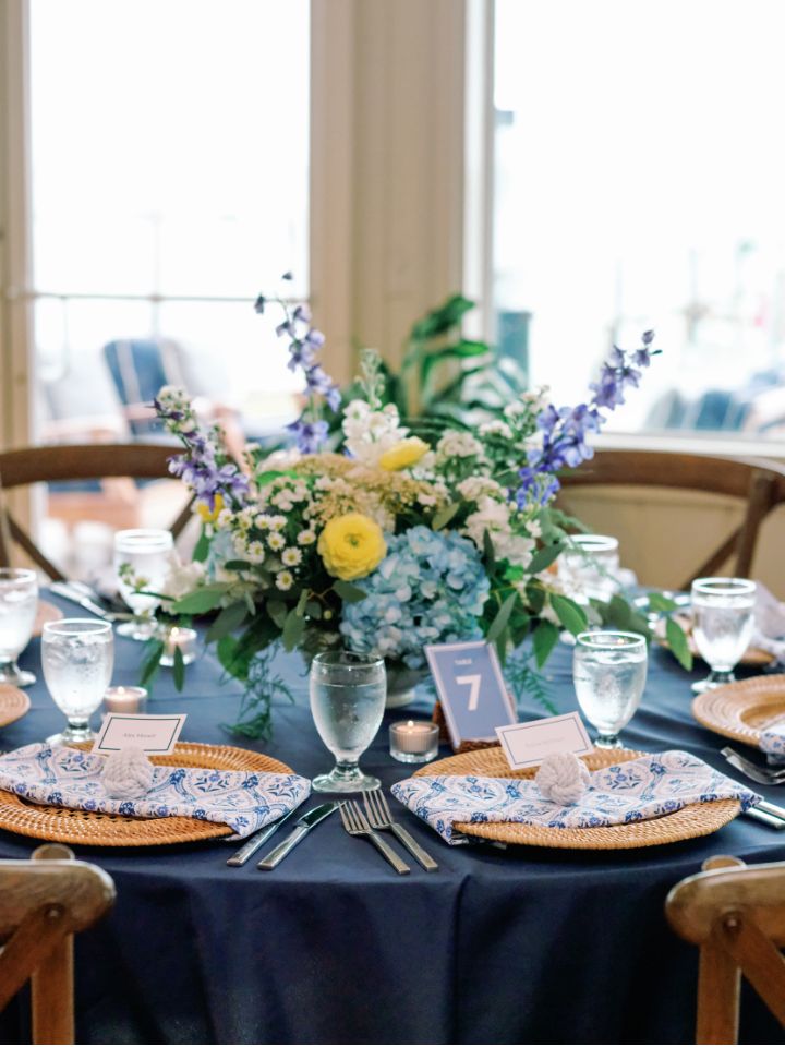 White compote bowl with flower arrangement on a guest table.