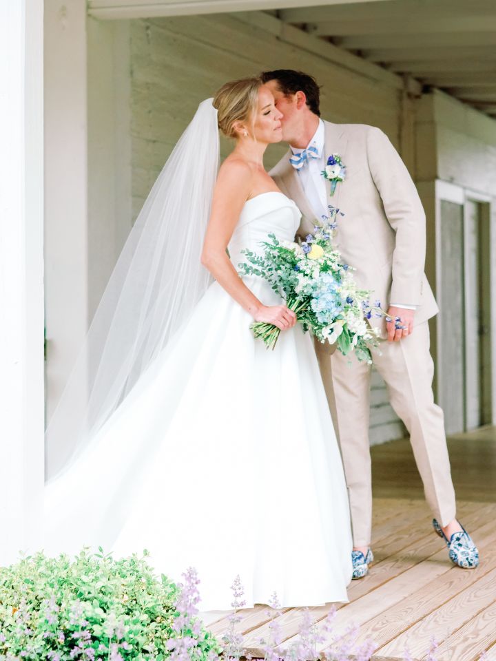 Bride and groom kiss while holding floral bouquet.