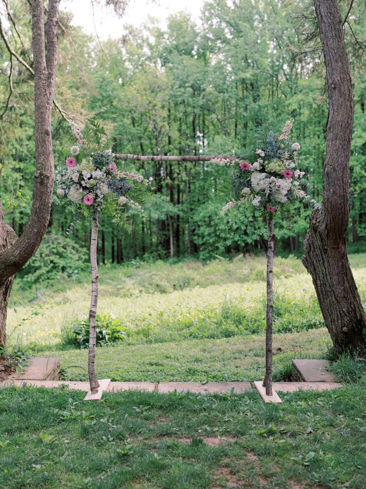Rustic style branch wedding arch has two floral arrangements, one at each corner.