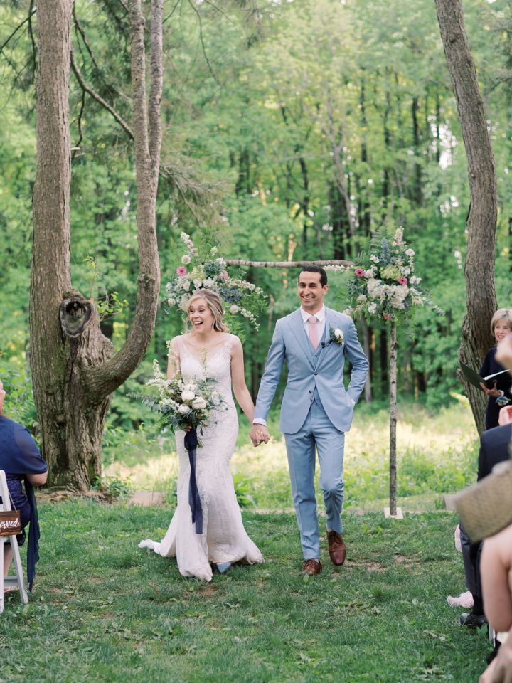 Bride and groom walk down the aisle after their ceremony in a wooded natural area.