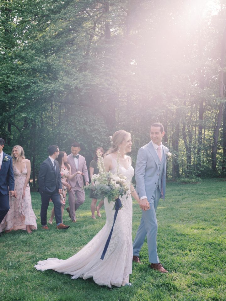 Bride and groom walk through a field with their wedding party.
