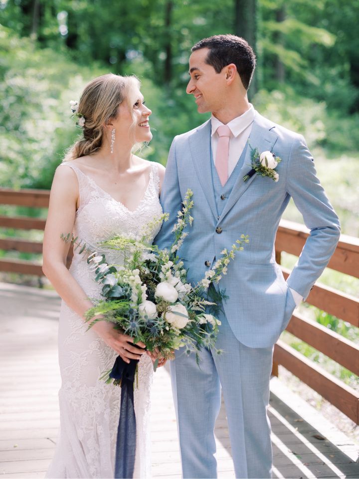 Bride and groom smile at each other, holding her bridal bouquet.