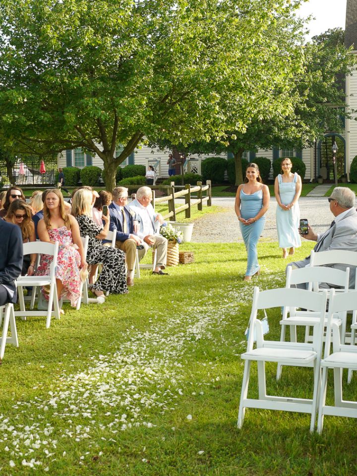 aisle petals Bridesmaids walk down grass aisle at outdoor ceremony with white flower petals.