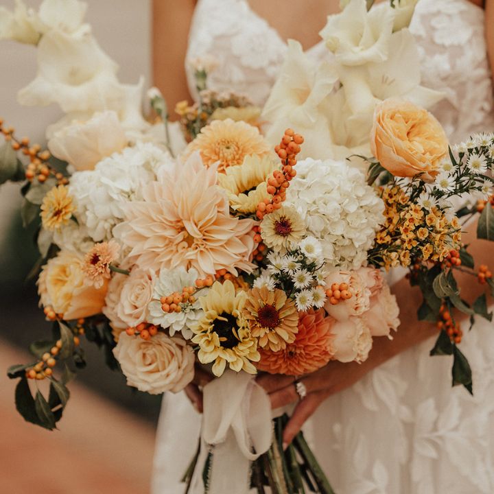 Bride holds sunset pastel bridal bouquet with fall flowers.