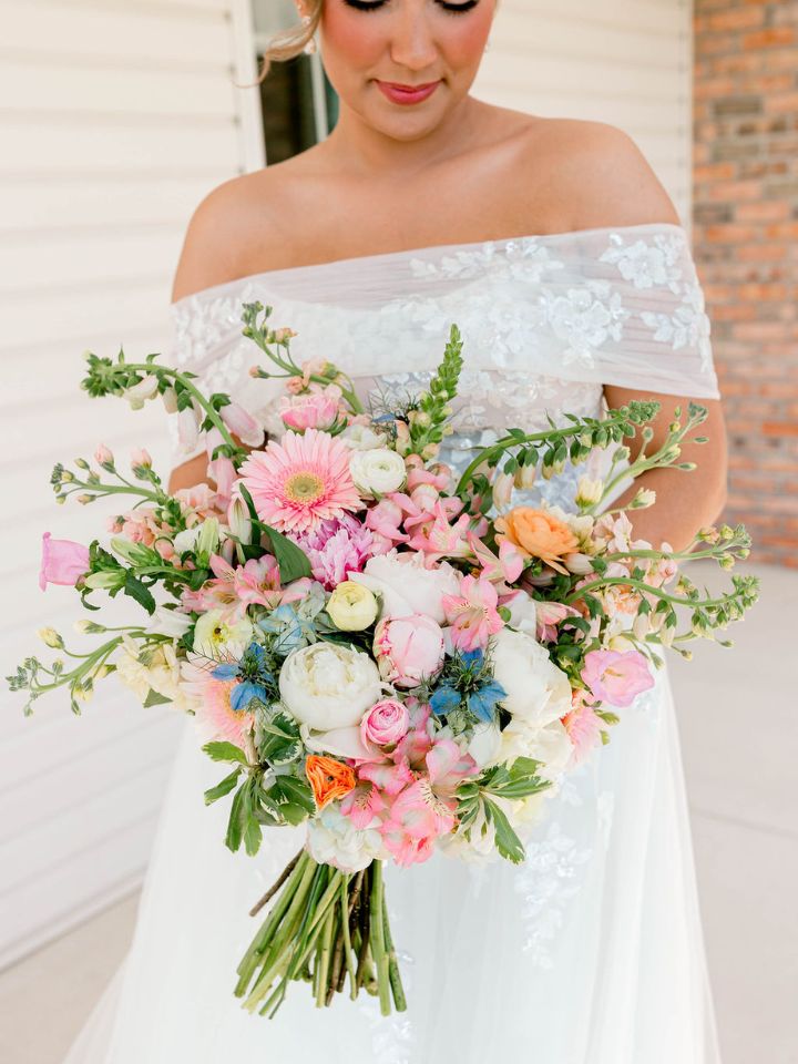 bailey classic one sided Bride smiles down at bouquet full of pastel spring flowers.