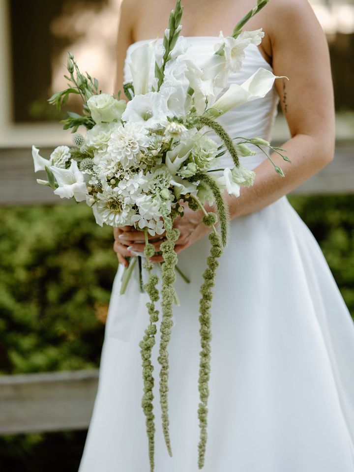 cascading petite cassi Closeup of bride in white, holding bouquet of flower farm white and green with cascading amaranth.