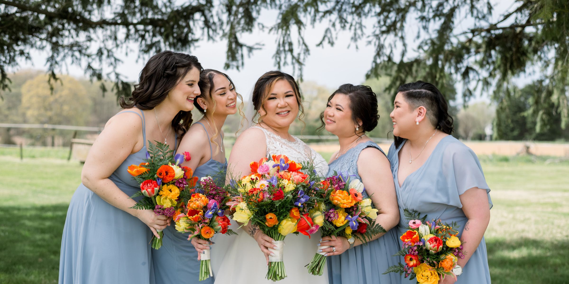 Bride smiles at camera surrounded by bridesmaids in dusty blue dresses.