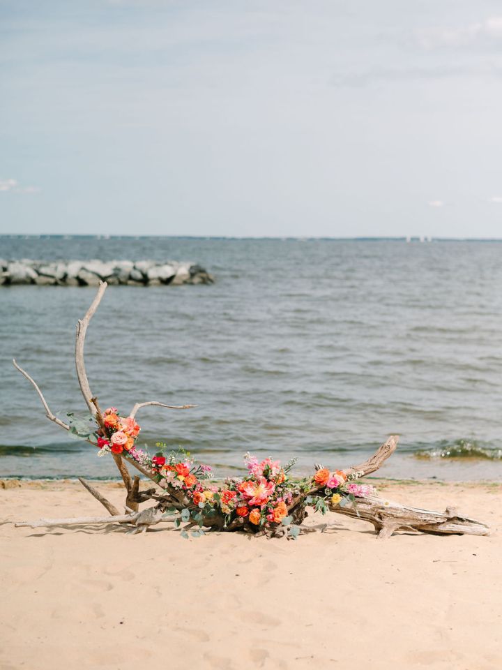 Driftwood ground arch on a beach wedding with coral pink flowers.