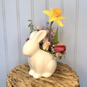 Ceramic rabbit container sits on a basket and holds spring flowers