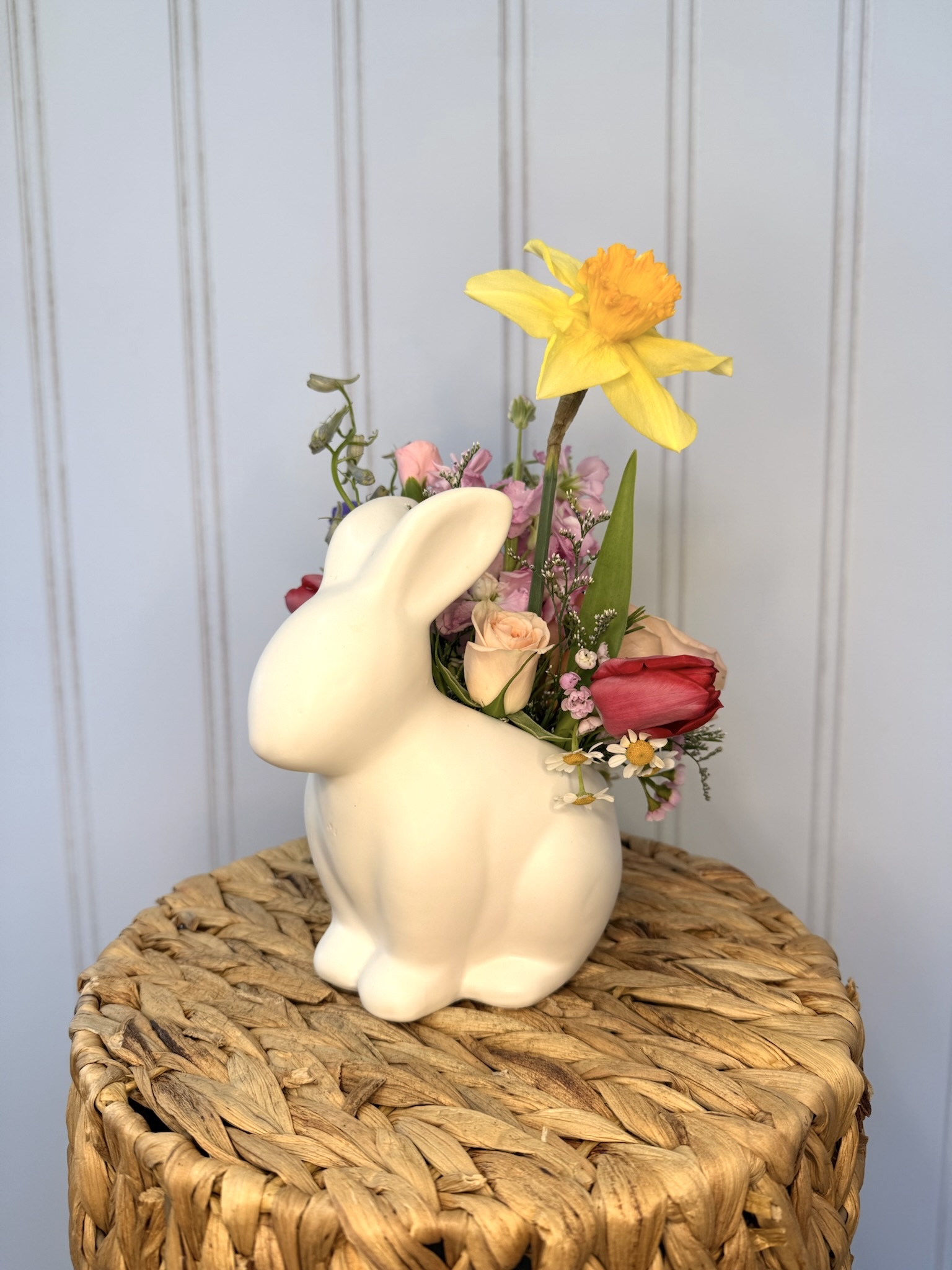 Ceramic rabbit container sits on a basket and holds spring flowers