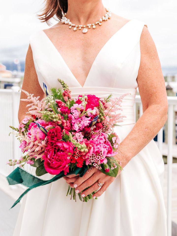 erin petite onesided Bride holds a petite bouquet in all shades of pink, with an emerald green ribbon.
