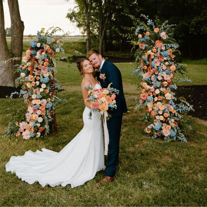 Pastel flowers fill two floral columns for a wedding ceremony, on either side of bride and groom.