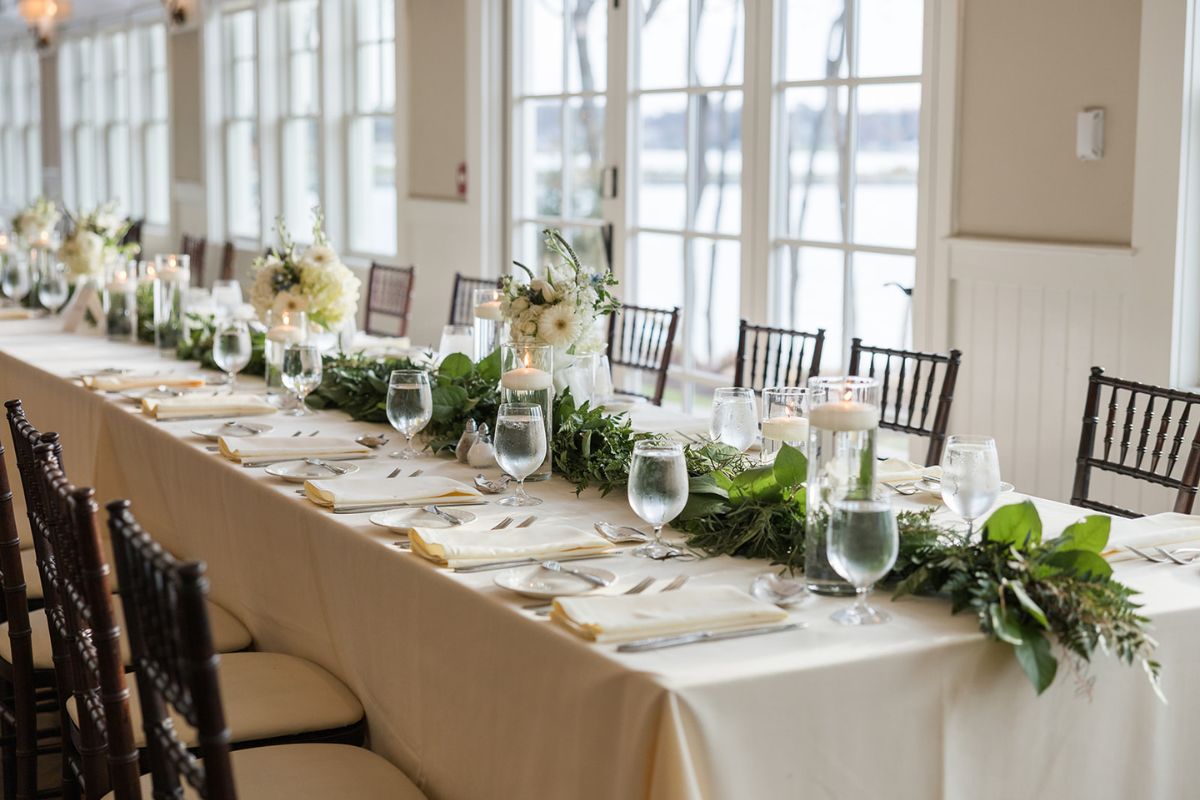Greenery garland at a long head table with white linens, with floating candles.