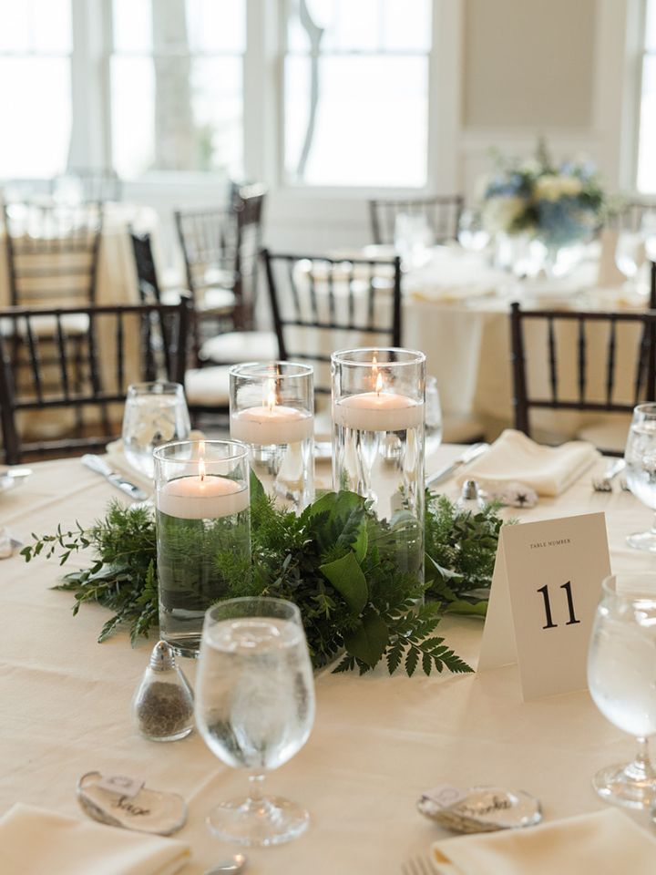 Trio of mixed height glass cylinders with white floating candles, surrounded at the base with mixed greenery.