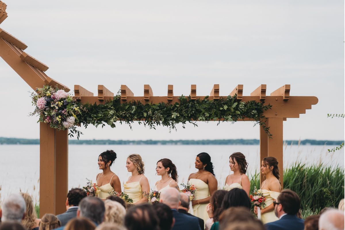 Bridesmaids stand under the arch at Herrington on the Bay, decorated with a garland.