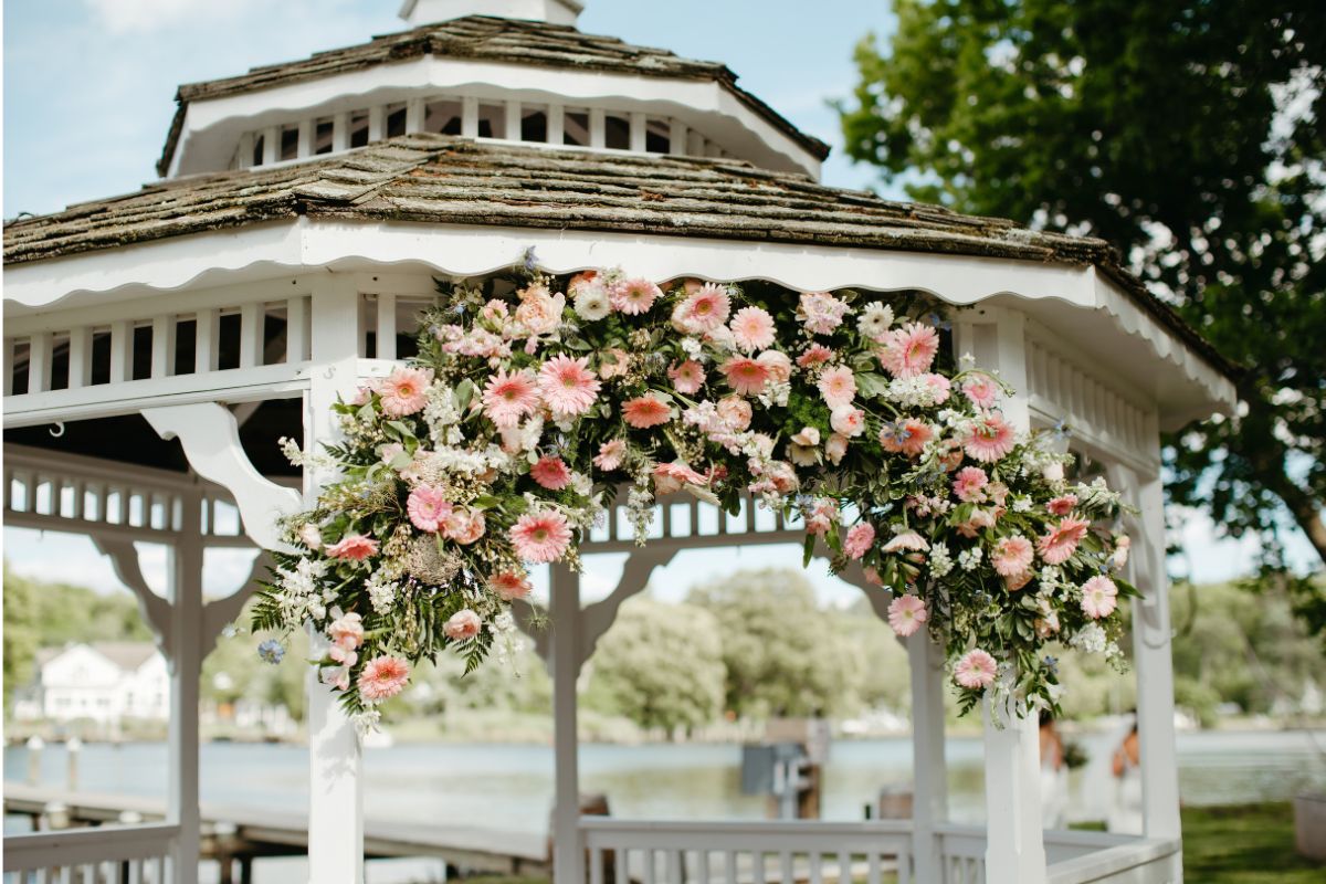 Waterfront wedding ceremony gazebo has pink flowers.