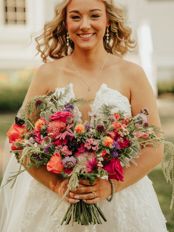 kirstie classic organic Bride smiles at camera holding a bouquet of bright summer flowers