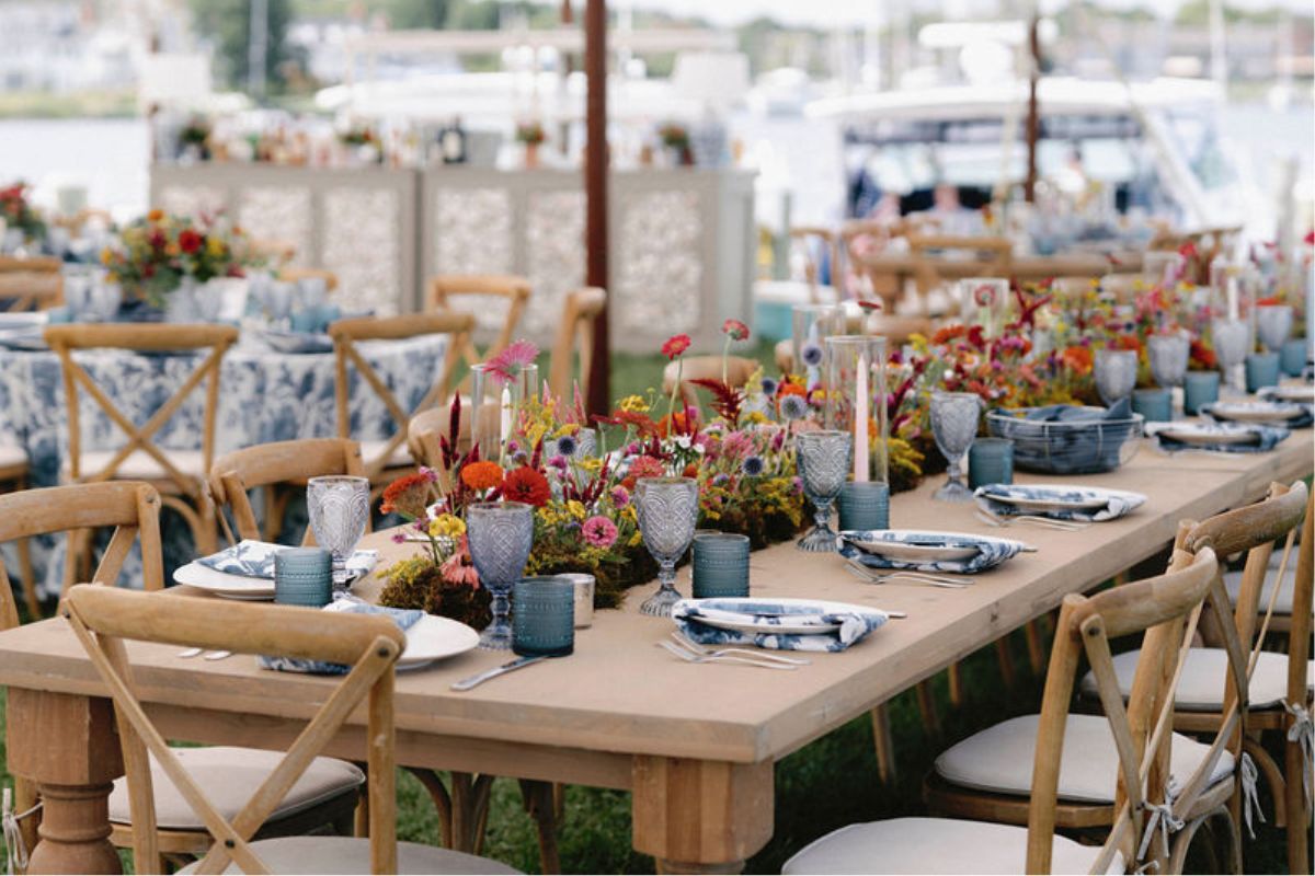 Moss runner with vibrant summer flowers in all colors, with blue and white decor details in place settings.