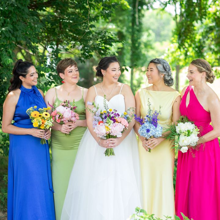 personals bouquets sq Bride stands with her bridesmaids in different bright colored dresses, holding colorful bouquets.