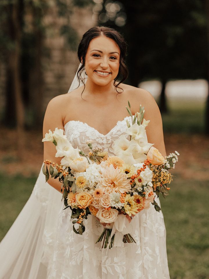 rachel classic one sided Bride smiles and holds her bouquet full of soft sunset pastel color florals.