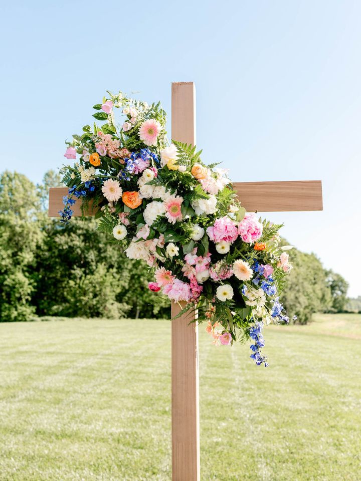 Wooden cross for outdoor wedding ceremony with colorful spring flowers.