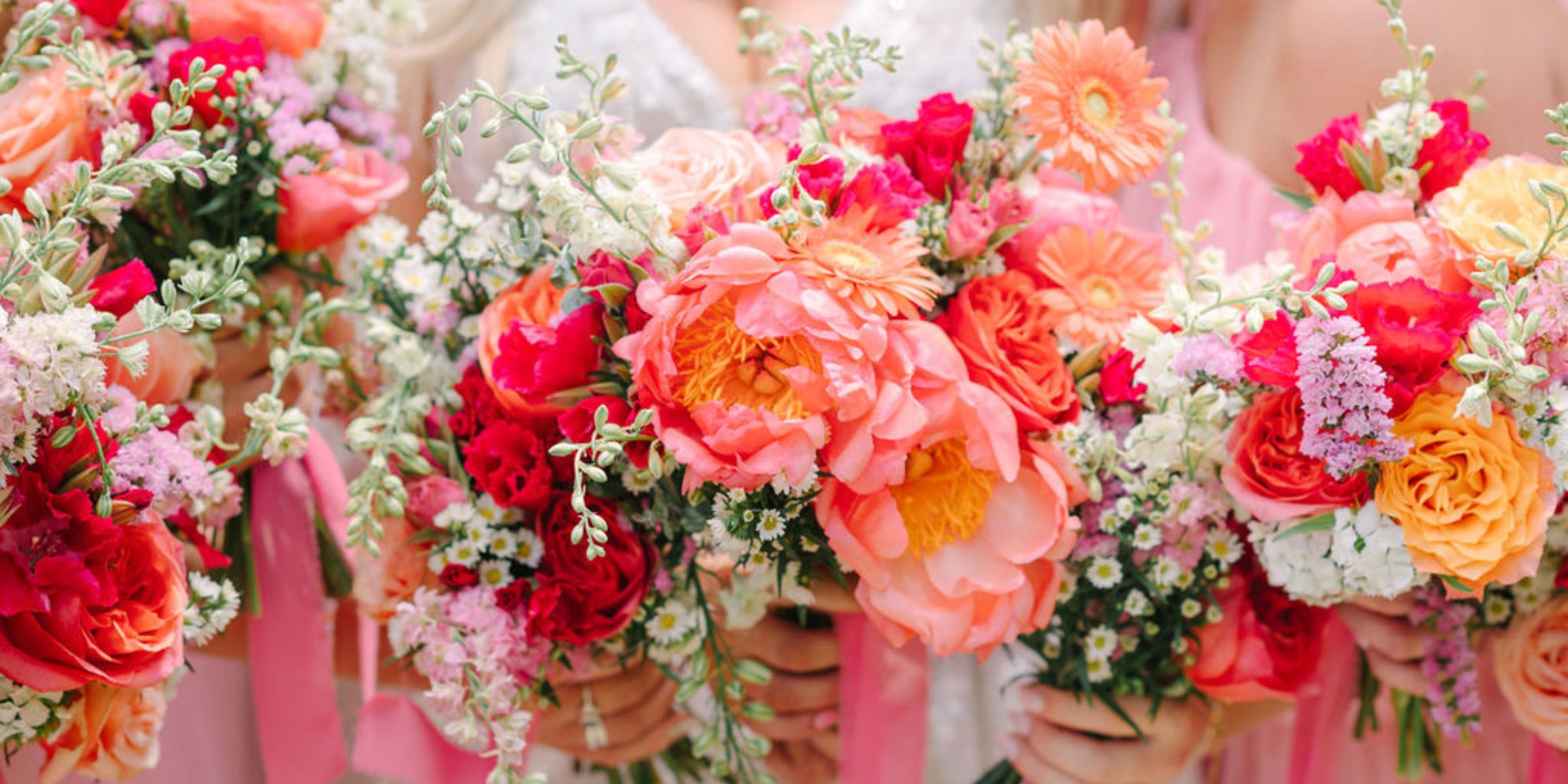 Bride and bridesmaids in bubblegum pink hold up pink, white, coral floral bouquets.