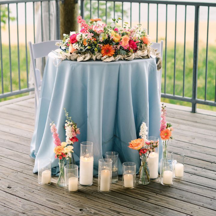 Blue tablecloth small sweetheart table with coral pink and orange flowers, and candles at the base.