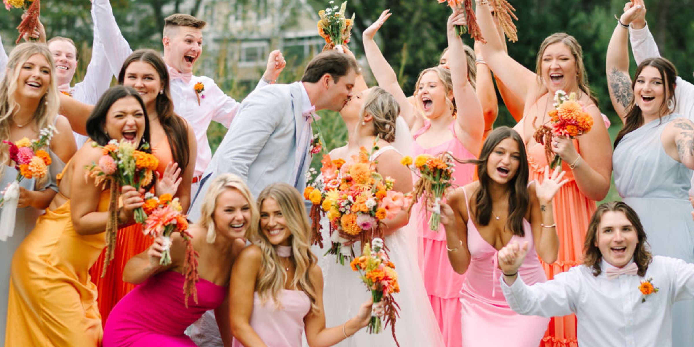 Wedding party cheers on bride and groom, in colorful dresses and flowers.
