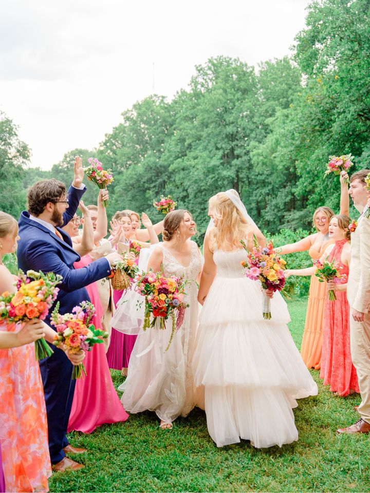 weddings page top Brides smile at each other while walking between cheering wedding party.