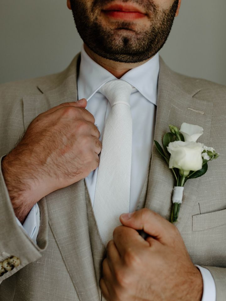 white simple boutonniere Groom wears khaki suit with white flower boutonniere.