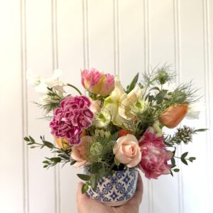 Hand holds a Chinoiserie flower arrangement in a blue and white ceramic dish.