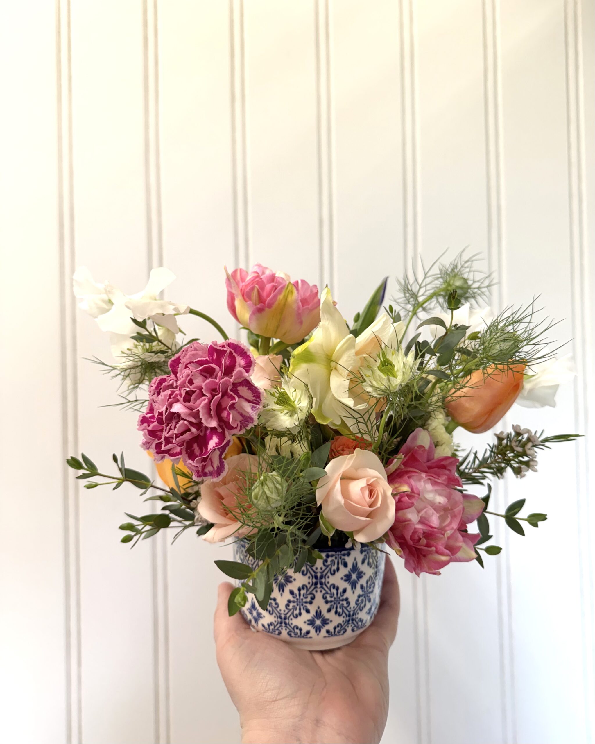 toy-store-20 Hand holds a Chinoiserie flower arrangement in a blue and white ceramic dish.