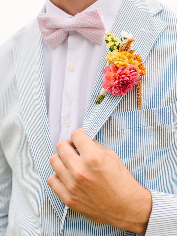 Closeup of groom's seersucker suit with pink bowtie and colorful boutonniere.