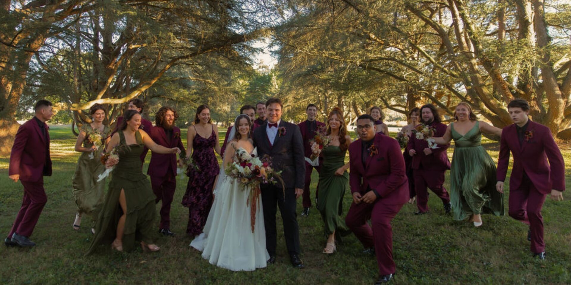 Bride and groom stand in wooded area with wedding party.