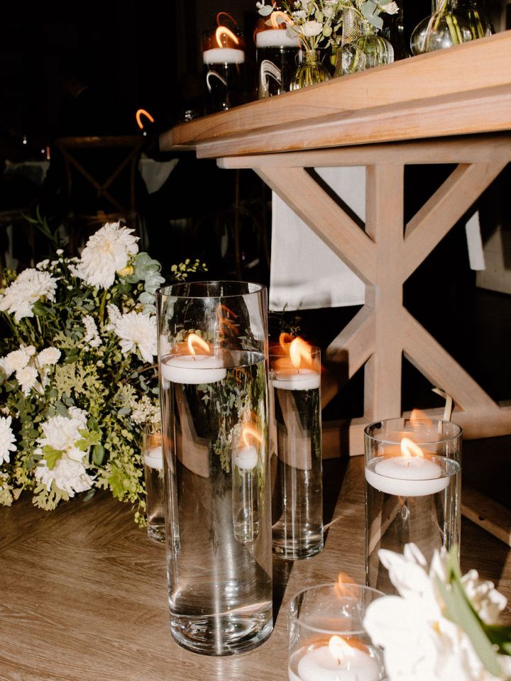 Floating candles in tall glass cylinders at night in front of sweetheart table.