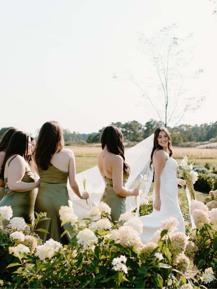 Bride smiles at bridesmaids as they walk through a hydrangea garden.