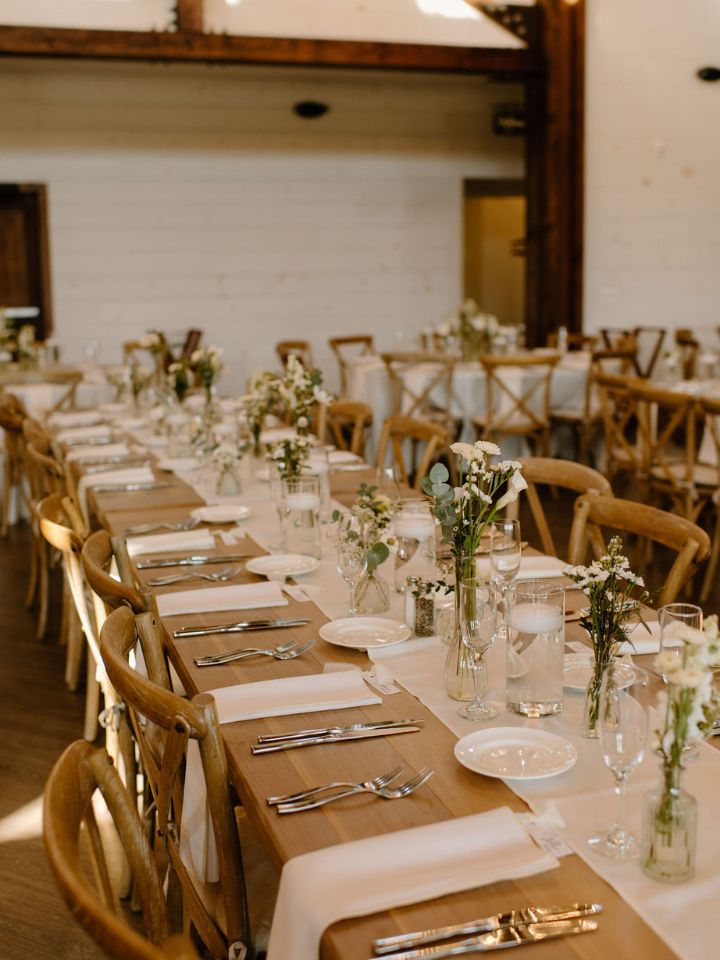 Rectangular guest table at a wedding reception with bud vases and candles.
