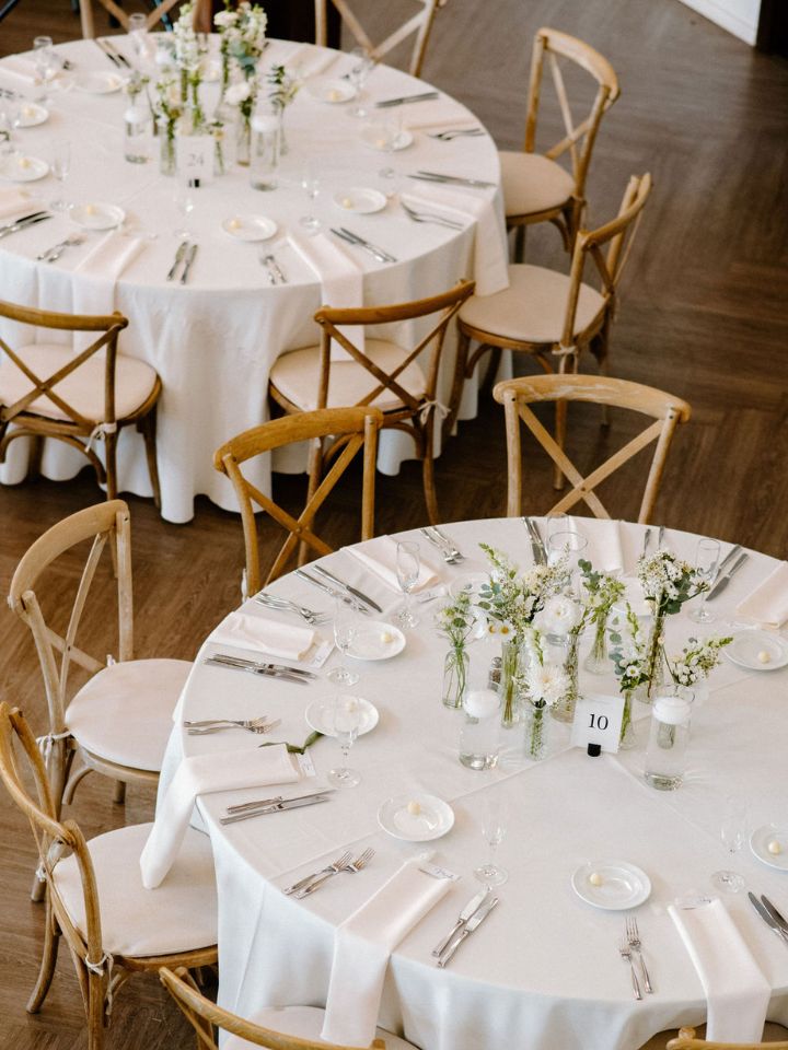 Round tables with white linens and centerpiece of bud vases and candles.