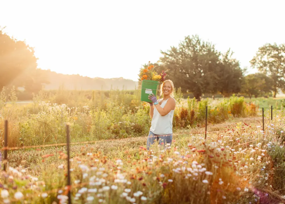 Lizzy standing in the flower field at Wildly Native Flower Farm holding a bucket of cut flowers and smiling at the camera